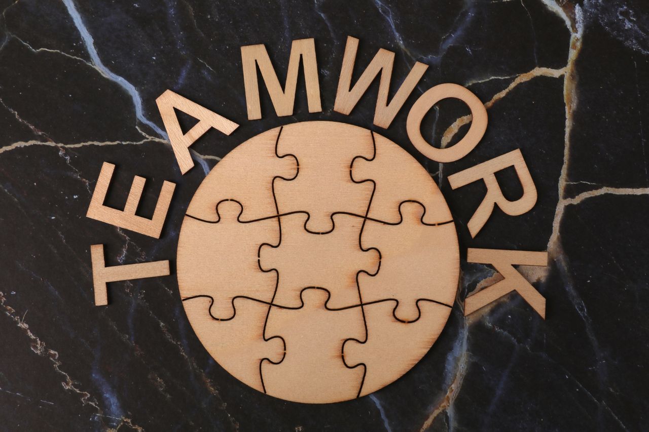 Wooden puzzle pieces arranged to spell teamwork, symbolizing collaboration on a marble background.