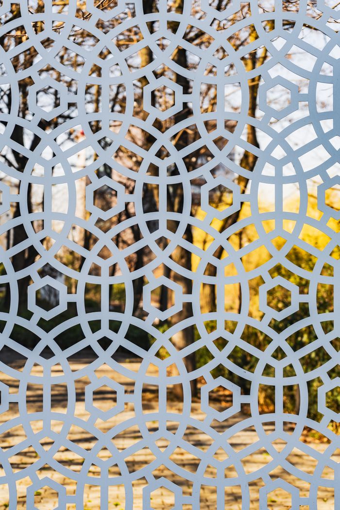 Decorative fence with geometric pattern reflecting picturesque autumn park with calm alley and yellow trees on sunny day