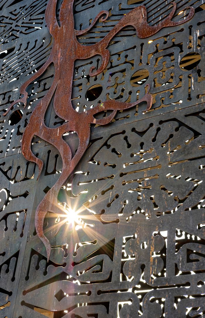 A detailed metal panel with an artistic cut-out design and sunlight peeking through.